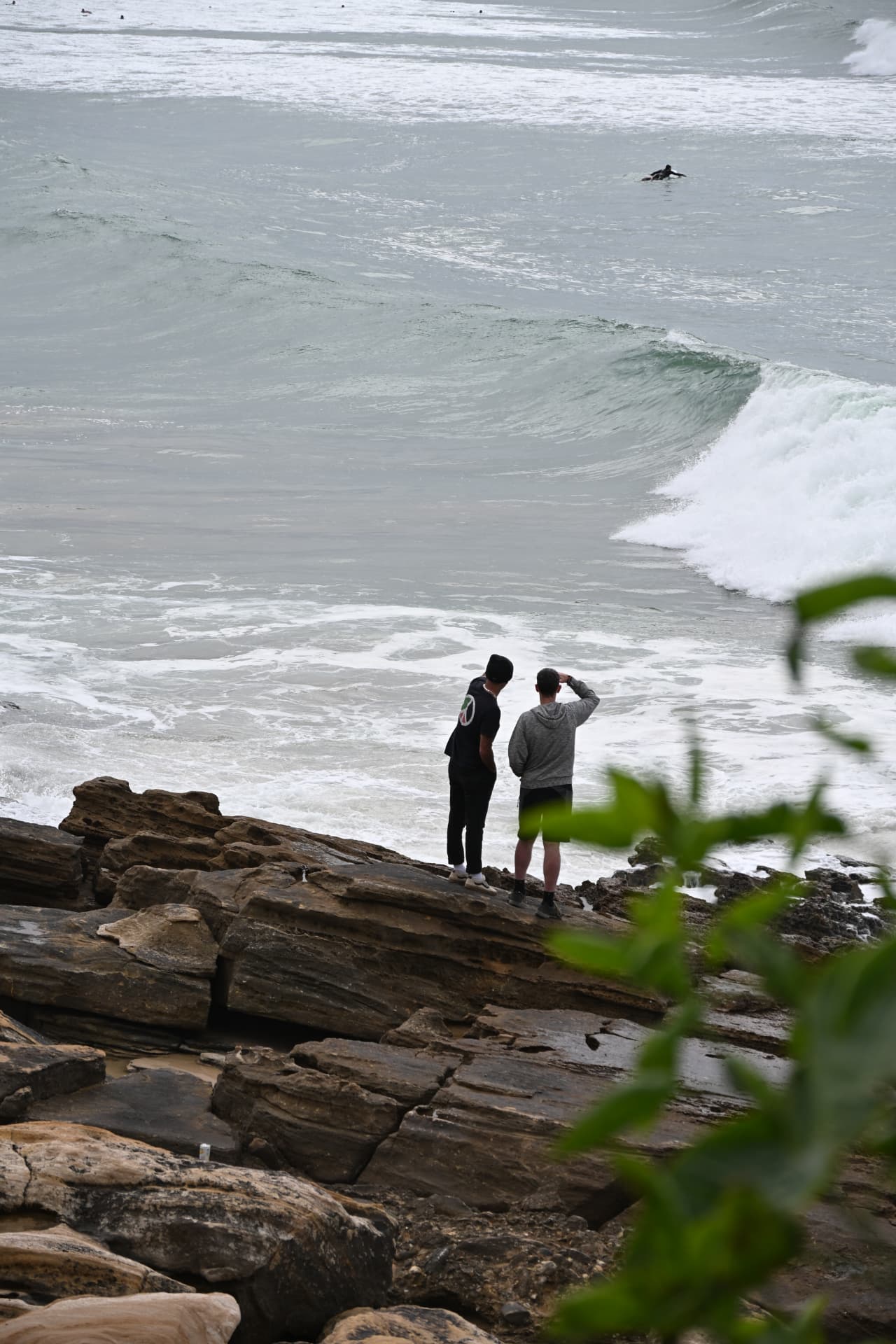 Twee surfers kijken naar de golven vanaf de rotsen