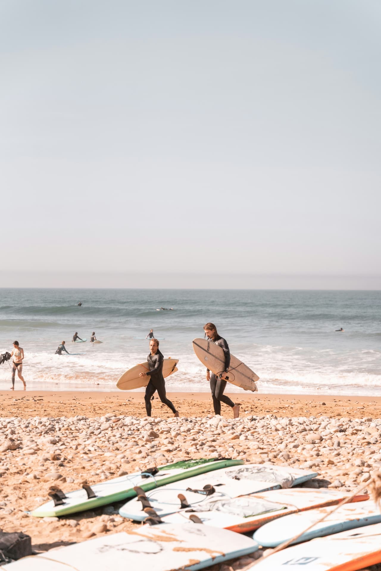Twee surfers met plank onder de arm lopen over het strand