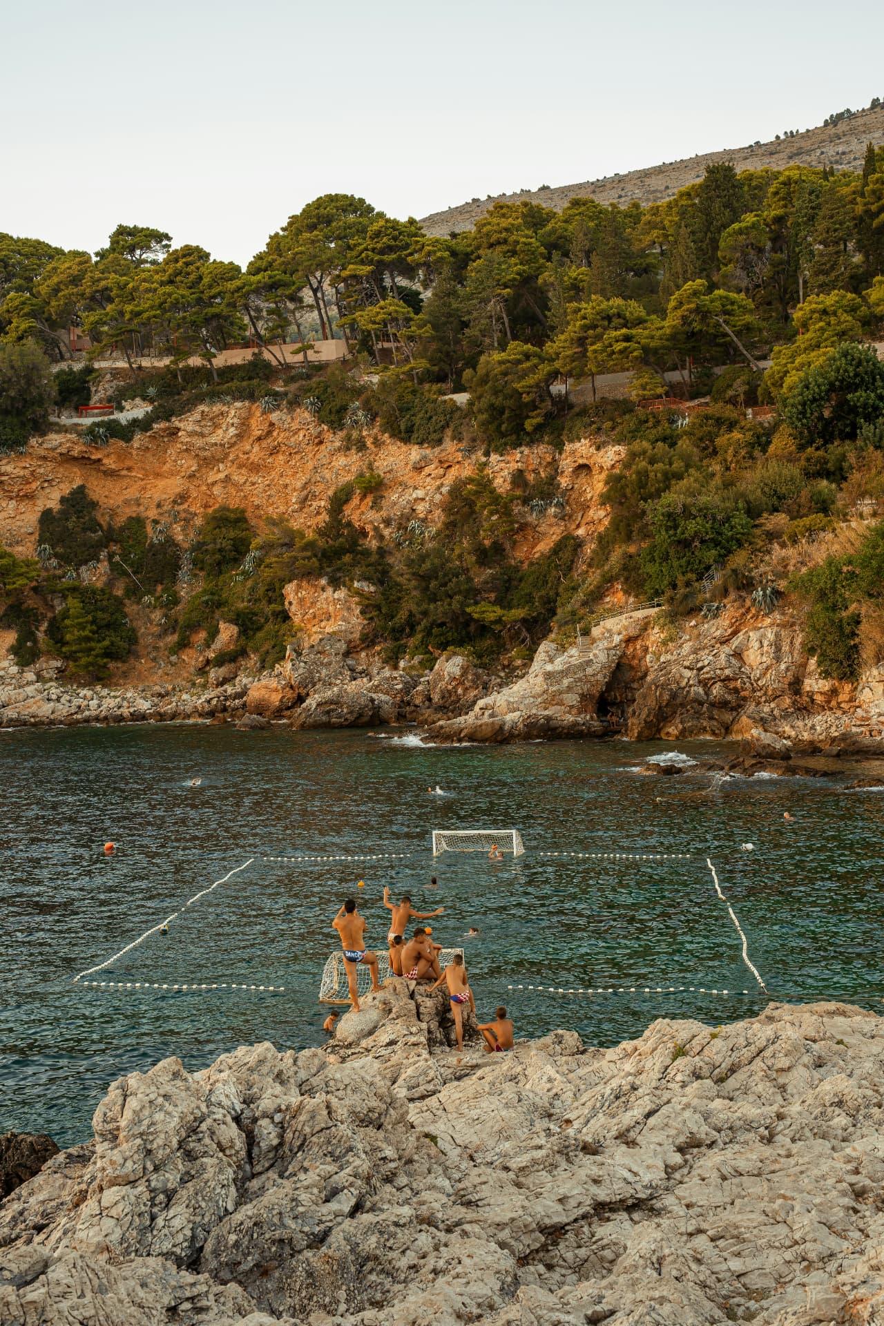 Mensen die van de rotsen in een baai zwemmen en waterpolo spelen