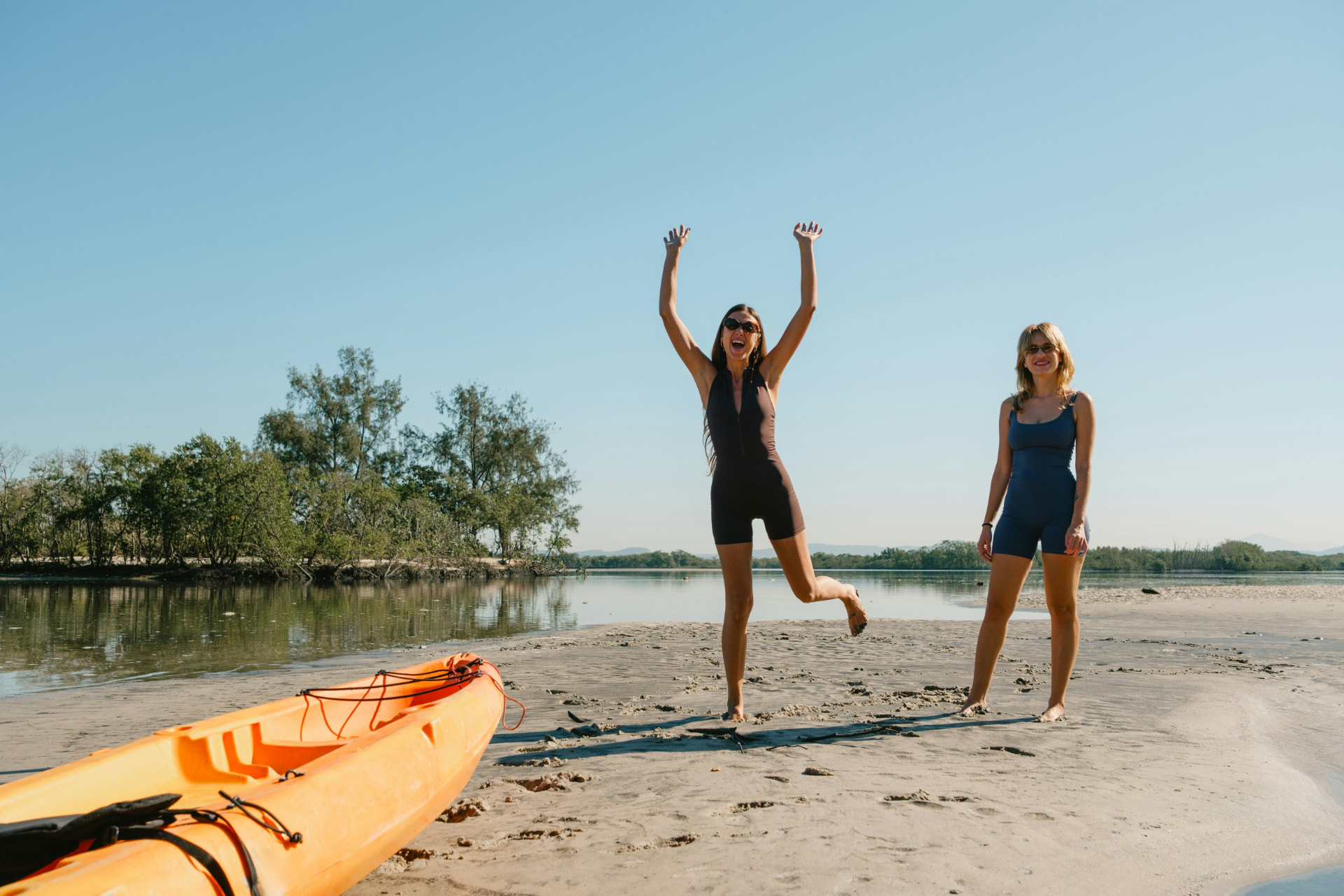 Twee vrouwen die juichend op een zandbank staan, met een oranje kajak naast hen