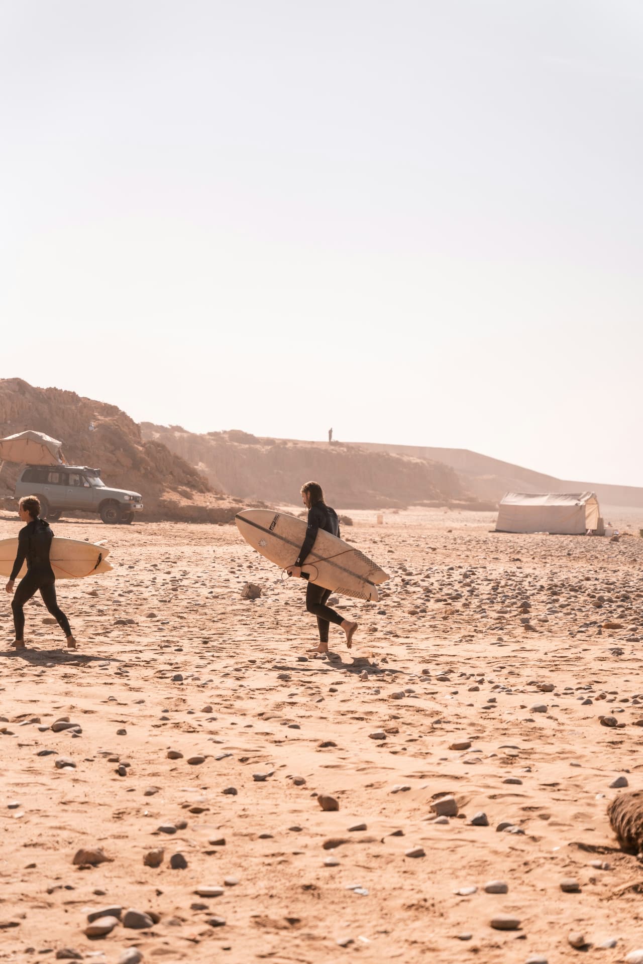 Twee surfers in wetsuit lopen met hun plank over het strand